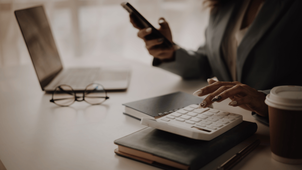 Persona utilizando una calculadora y teléfono móvil mientras organiza sus finanzas, representando cómo salir del endeudamiento mediante el uso de herramientas para gestionar deudas.