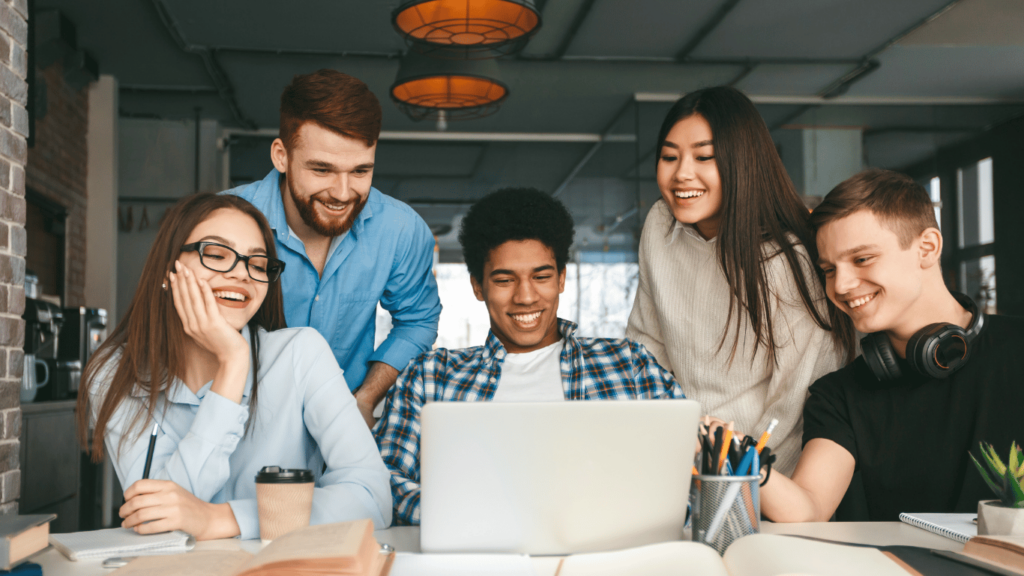 Grupo de jóvenes sonriendo mientras miran una computadora portátil, participando en un aprendizaje colaborativo, promoviendo la educación financiera con Educa tu Cartera, de Condusef.