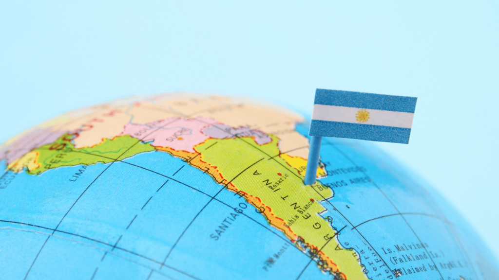 Un mapa del mundo con una bandera de Argentina clavada en el país, destacando su posición geográfica. Esta imagen representa la ubicación de Argentina como un destino clave para la Inversión Extranjera Directa en América Latina.